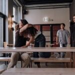 Friends sharing a warm hug while others arrive at a cafe