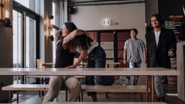Friends sharing a warm hug while others arrive at a cafe