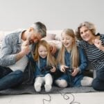 Grandparents and two granddaughters laughing while playing video games together at home