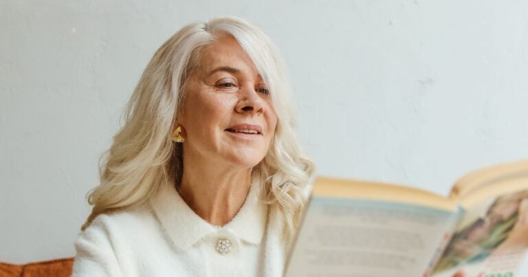 Woman with long gray hair absorbed in reading a book at home